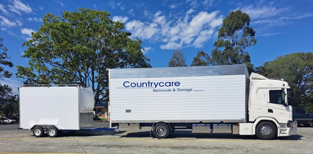 A profile view of a white Countrycare Removals & Storage truck with a matching white trailer parked in an asphalt lot.