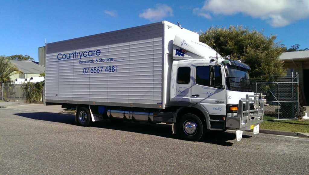 A white Countrycare Removals & Storage truck parked on an asphalt road under a clear blue sky.